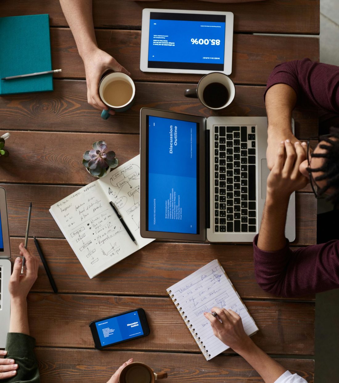 Group of coworkers discussing business strategies with laptops and tablets in a modern office setting.